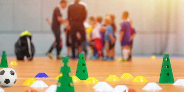 Indoor soccer training with cones and kids in the background.