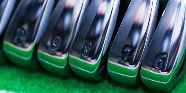 Close-up of shiny golf irons numbered 6 to 9 on green turf.