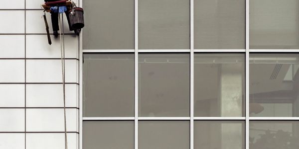 A window cleaner suspended by ropes cleans a tall building's exterior windows.