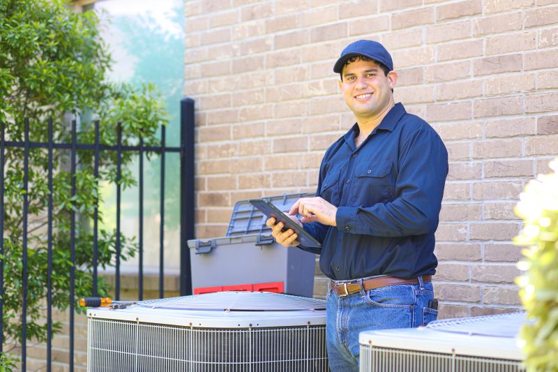 Latin descent blue collar air conditioner repairman working at residential home.  He prepares to begin work by gathering appropriate tools and referring to digital tablet.