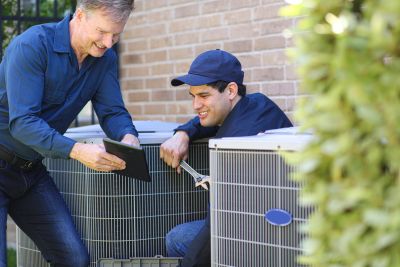 Technician and homeowner inspecting air conditioning unit with tablet and tools.