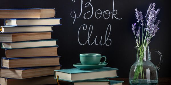 Books stacked with a cup and lavender flowers, with 'Book Club' written on a chalkboard.