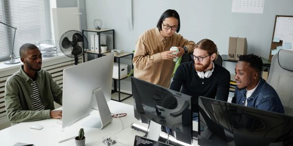 Gruppo di colleghi lavora insieme su computer in ufficio moderno.