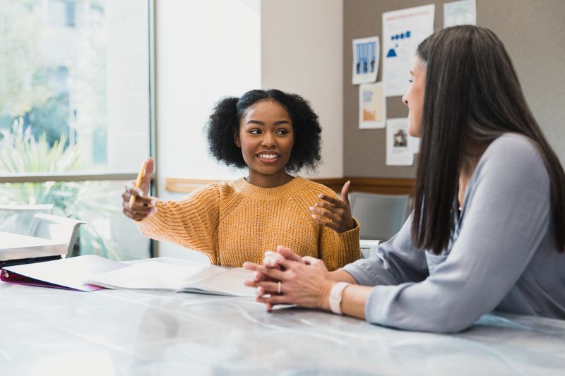 The teenage girl gestures as she explains something to her mid adult female teacher.