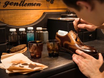 A craftsman carefully polishing a brown leather shoe with a brush.
