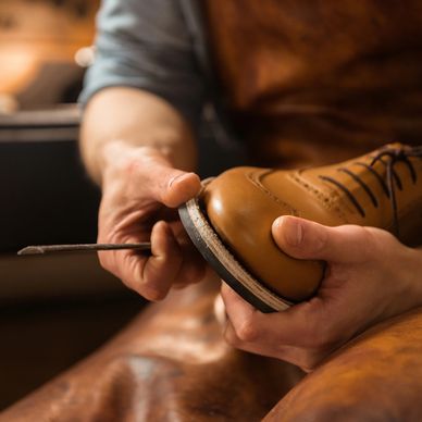 A craftsman repairs a tan leather shoe using specialized tools.