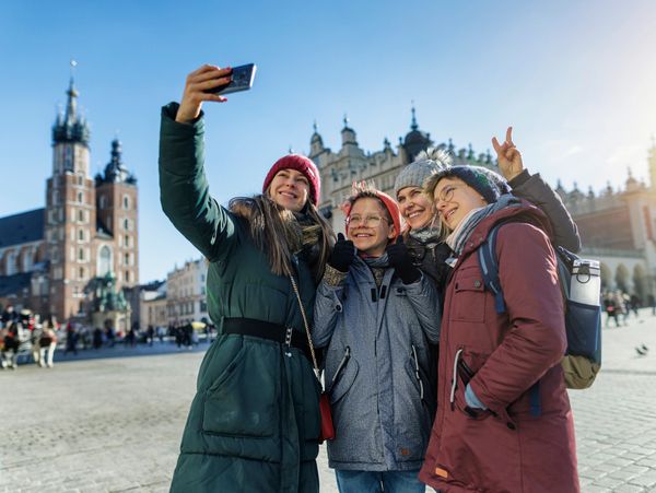 Four friends wearing winter coats take a selfie in a historic city square.