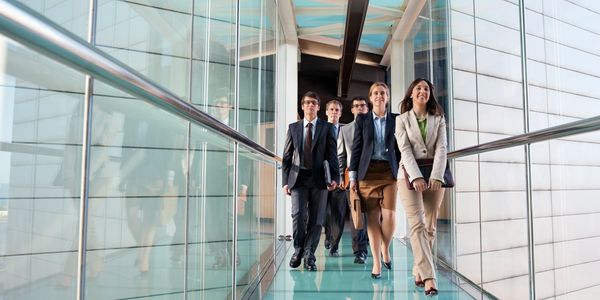 A diverse group of professionals confidently walking through a modern glass corridor.