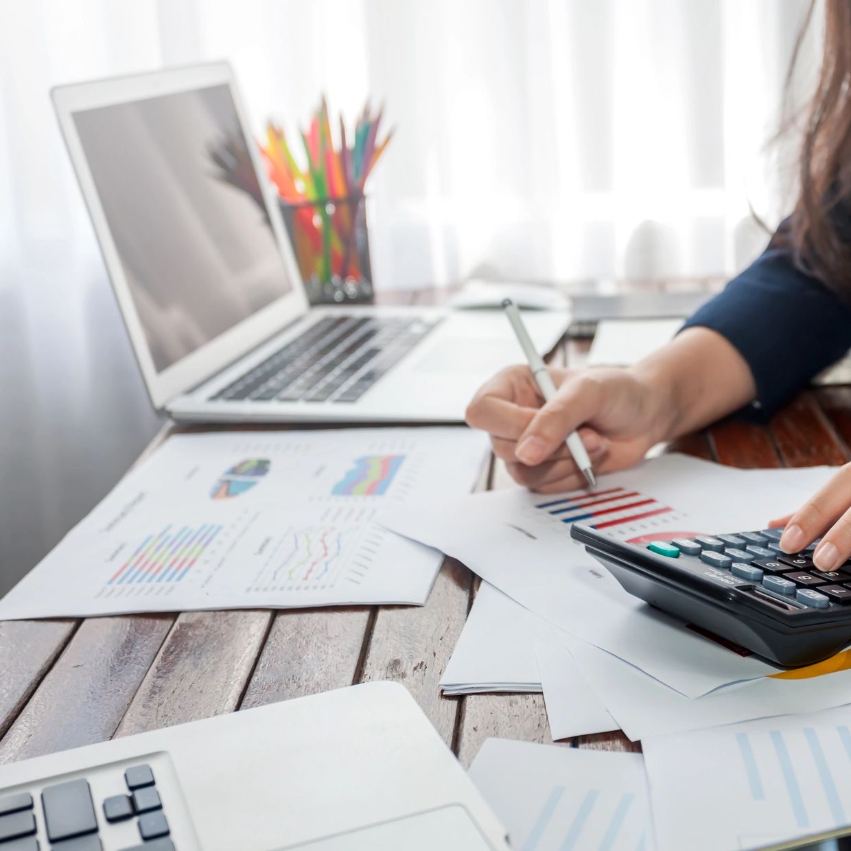 A person in business attire calculating finances with a calculator and charts.