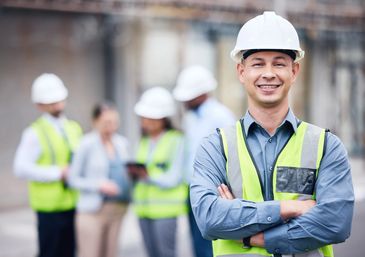 Smiling construction worker in a safety vest and helmet with colleagues in the background.