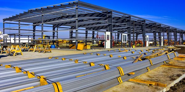 Steel framework structure under construction with bundled metal pipes in the foreground.