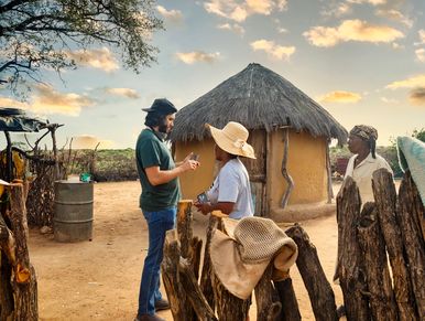 Two tourists and a local near a traditional hut.