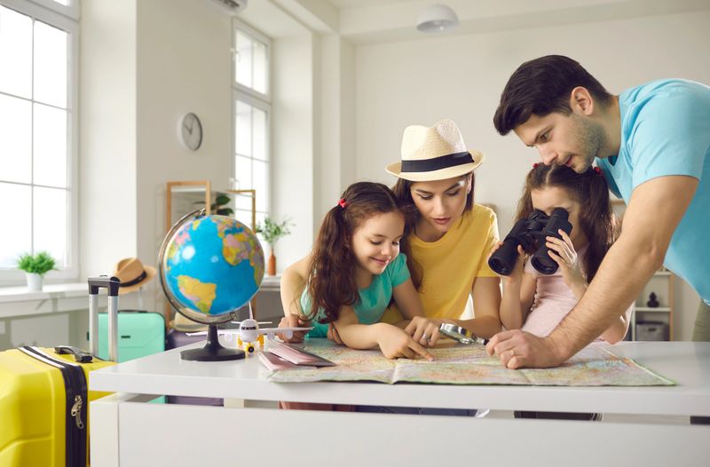 Family vacation planning, worldwide travelling, booking flight ticket. Happy mother and father with daughter children searching tourist route on paper map, choosing country to travel, tropical resort