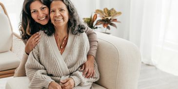 A daughter embraces her mother lovingly on a cozy sofa.