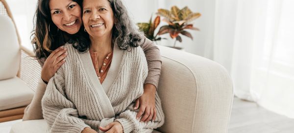 Two women smiling while embracing on a couch.