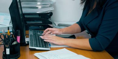Person typing on a keyboard at a cluttered office desk.