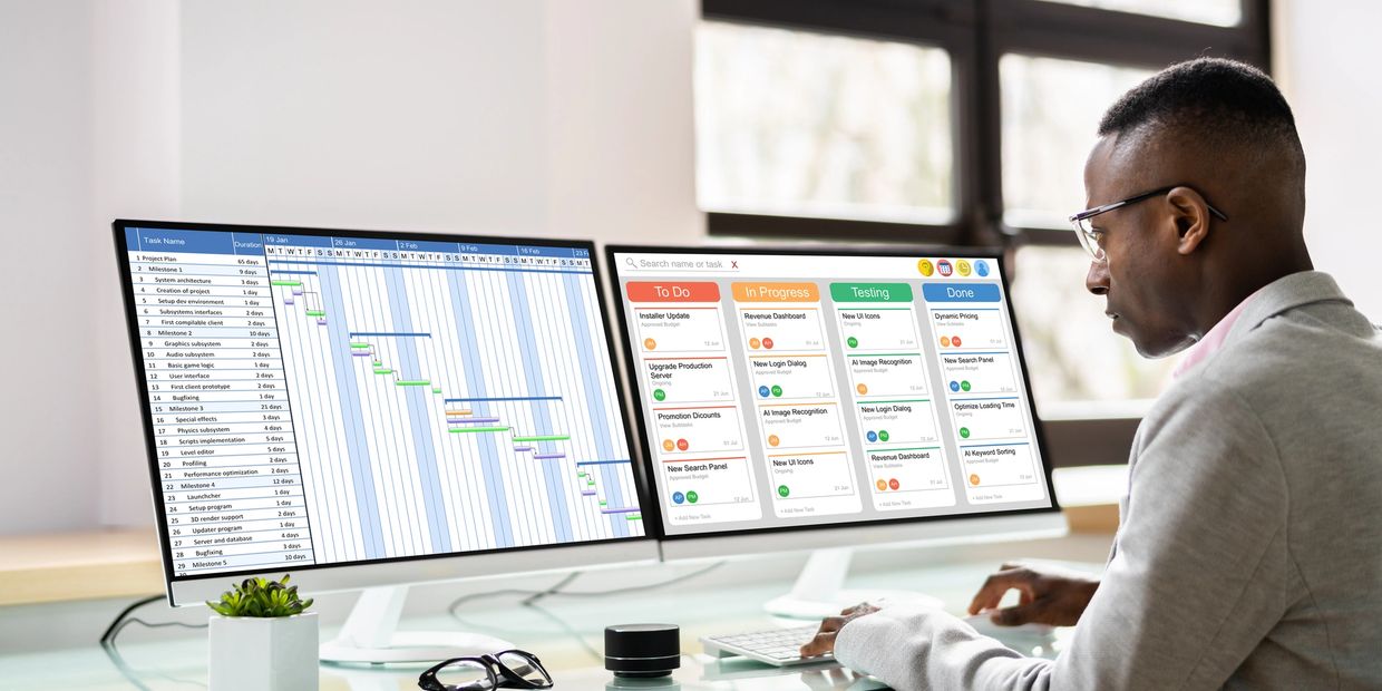 Man working with dual monitors displaying project plans and task boards.