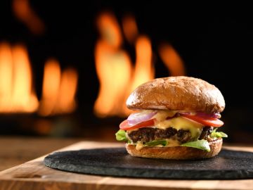 A cheeseburger with lettuce and tomato in front of a fire.