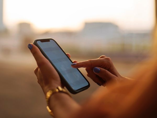 Person using a smartphone with a blurred background at sunset.