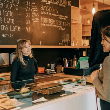 Barista smiling at a customer in a cozy café with a chalkboard menu.