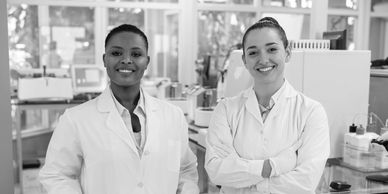 Two smiling female scientists in lab coats in a laboratory.