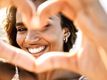 Woman smiling through a heart shape formed by her hands.