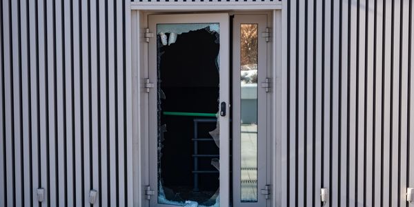A door with shattered glass and broken pieces scattered outside.
