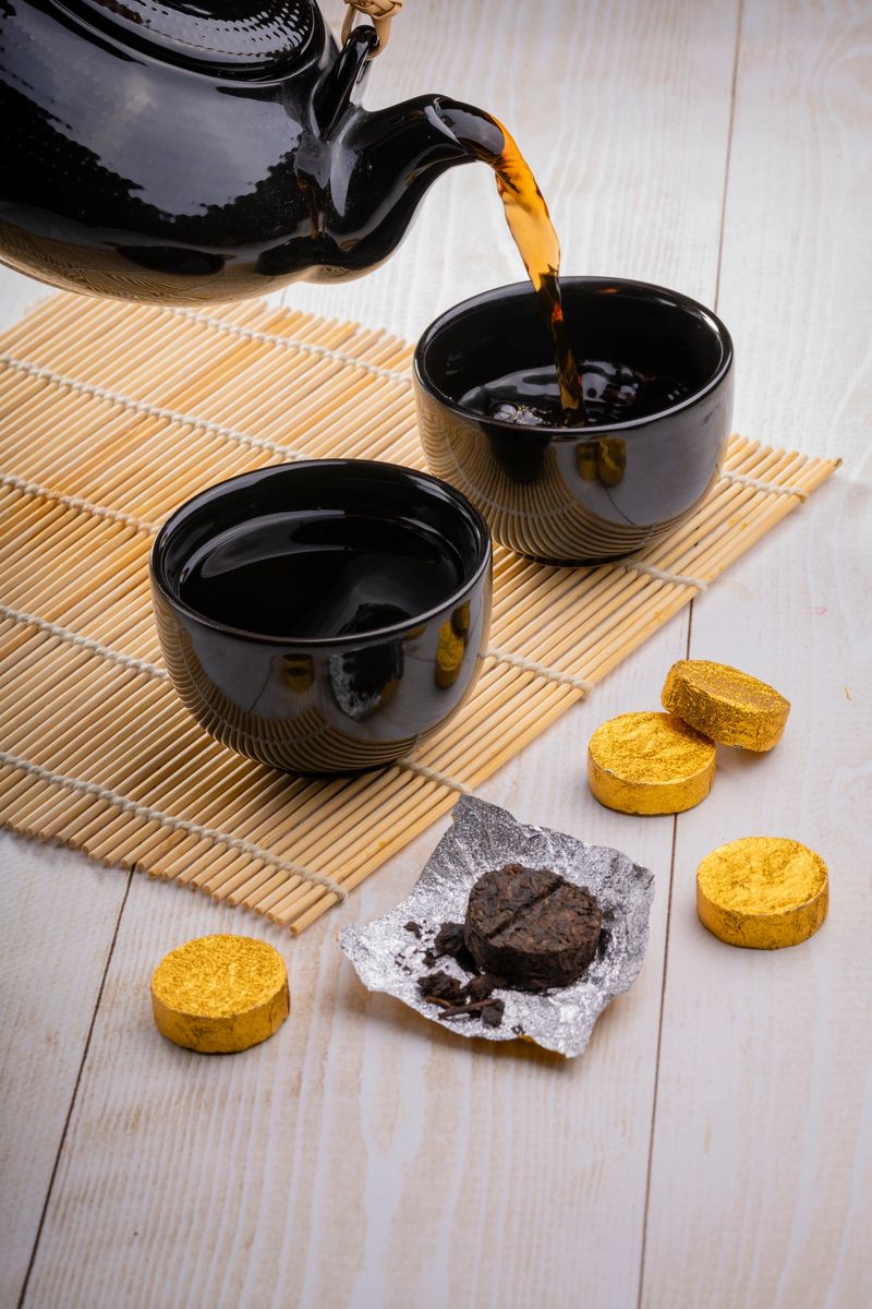 Black Chinese fermented Pu-erh tea. Black ceramic cups and teapot, bamboo mat, pressed pu-erh tea tablets. Close-up, selective focus.