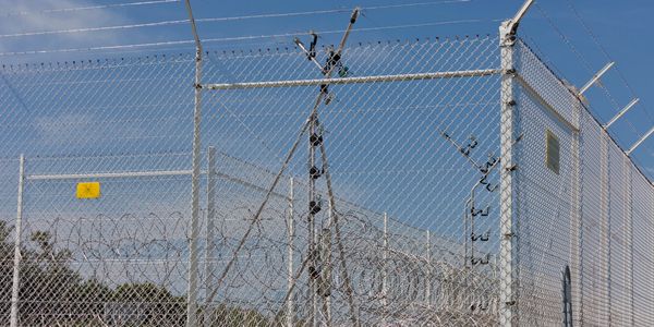High-security barbed wire fence topped with electric wires under clear blue sky.