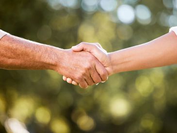 A close-up of two people shaking hands outdoors with a blurred background.