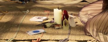 A candle and tarot cards arranged on a woven mat, with a person sitting nearby.