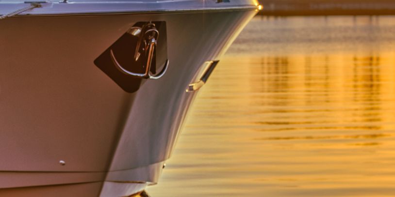 Close-up of a yacht's bow with an anchor at sunset by palm trees.