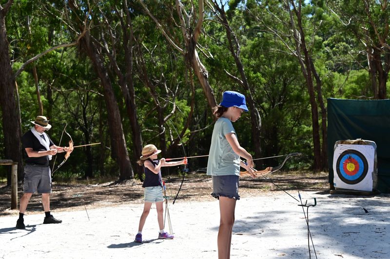 Father and daughters practicing archery together in the forest.
