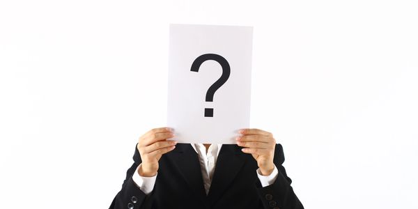 Person in black suit holding paper with question mark covering face.