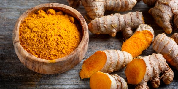 Wooden bowl of turmeric powder and fresh turmeric roots.