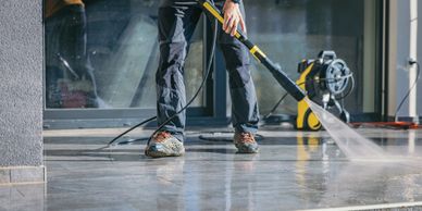Person power washing a concrete floor outside a building.