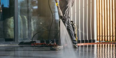 Person pressure washing the exterior of a white house with blue trim.