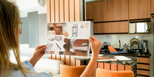 A woman holding an interior design mood board in a modern kitchen.