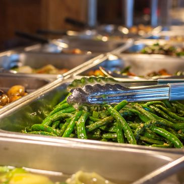 Fresh green beans served in a buffet tray with tongs.
