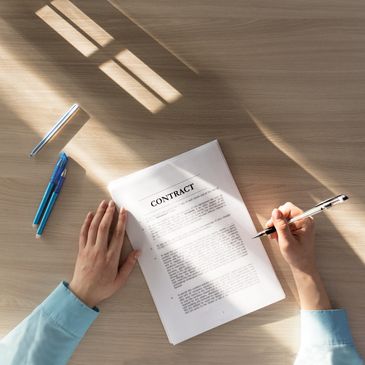 Person signing a contract on a wooden table with sunlight.
