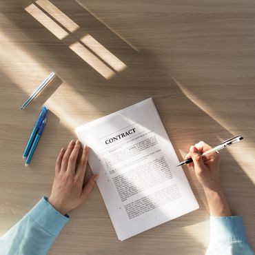 Person signing a contract on a wooden table with natural light and three pens.