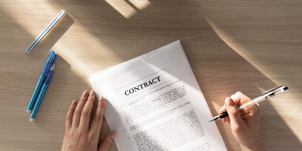 Person reviewing and signing a contract document at a sunlit wooden desk.