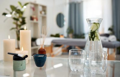 Spa setting with candles, cucumber water, and skincare products on a glass table.