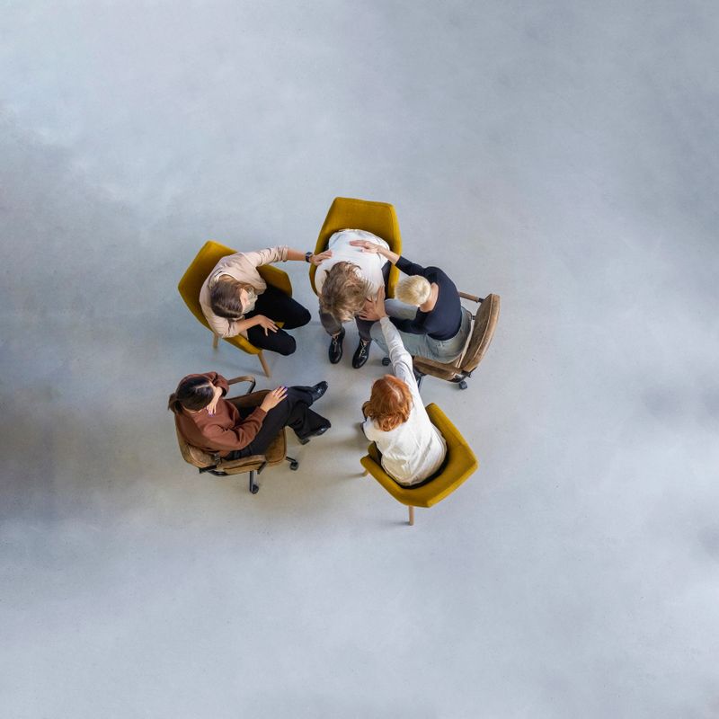Woman sharing struggles during support group meeting with people sitting by comforting her. People supporting a female member in a mental health therapy session.