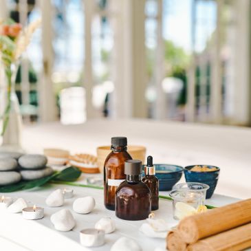 Spa essentials with bottles, candles, and stones on a white table.