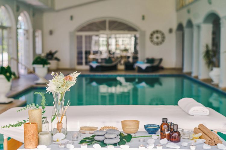 Spa setup with candles, stones, and flowers near an indoor pool.