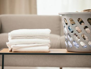 Folded white towels on a table next to a laundry basket filled with clothes.