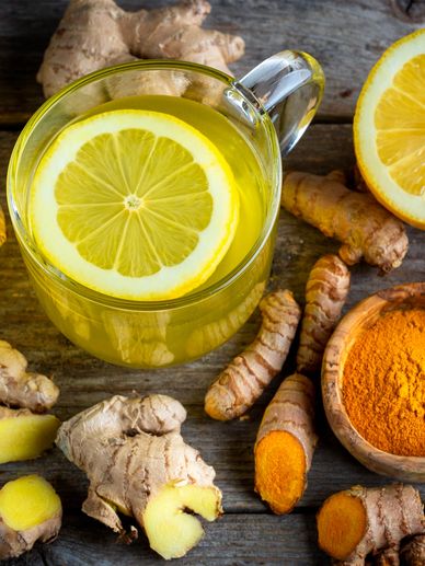 A cup of lemon ginger tea surrounded by fresh ginger, turmeric roots, and lemon halves.
