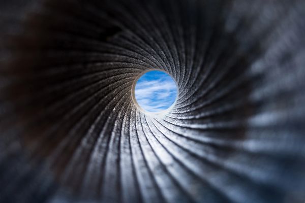 View through a textured tube revealing a blue sky with clouds.