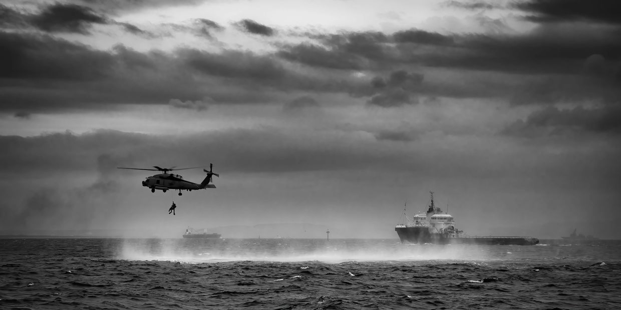 Helicopter performing a rescue or training operation over the sea near ships.